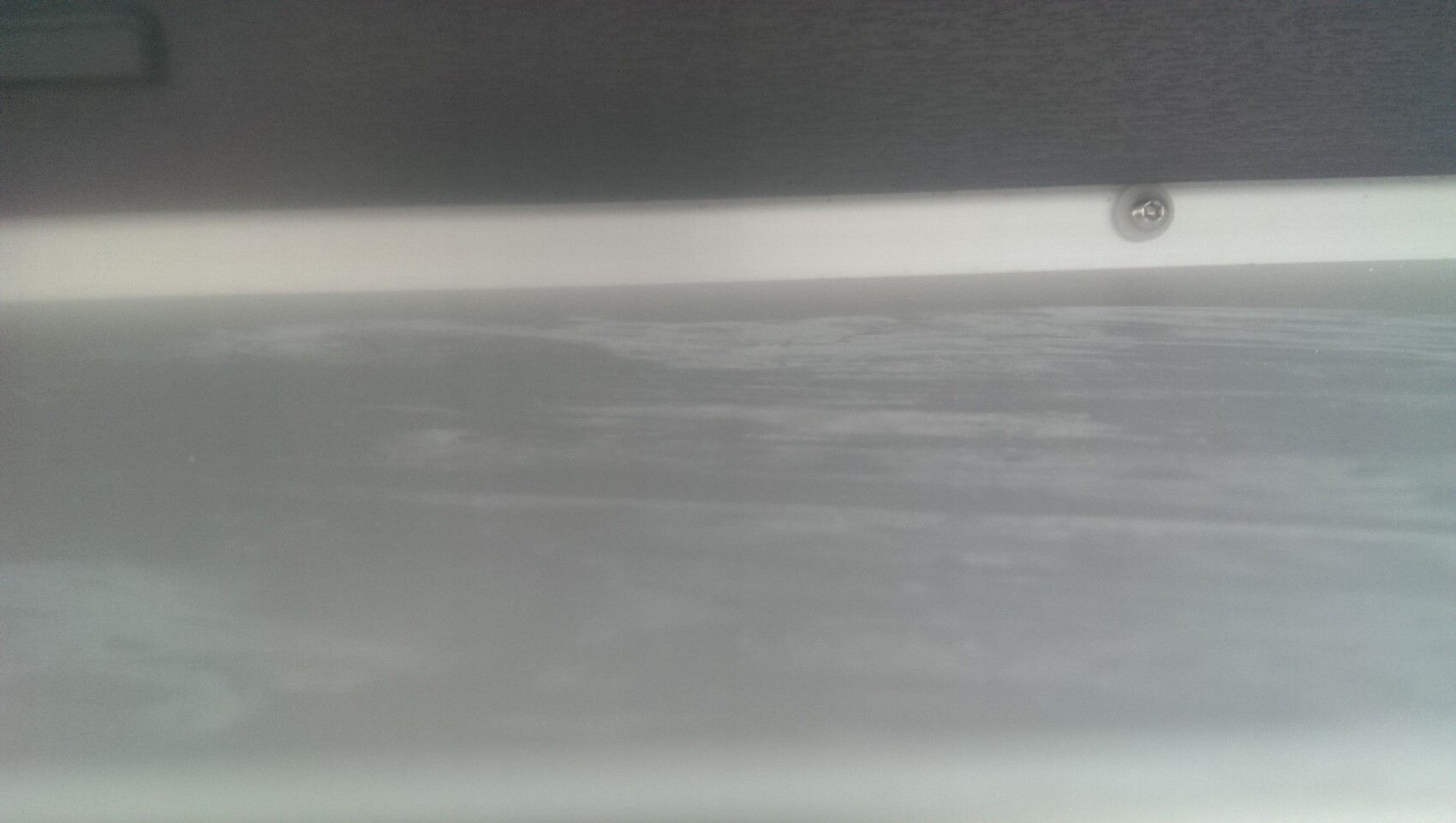 Nahaufnahme einer Metallkante mit Schraube und heller Leiste, unscharfer Hintergrund