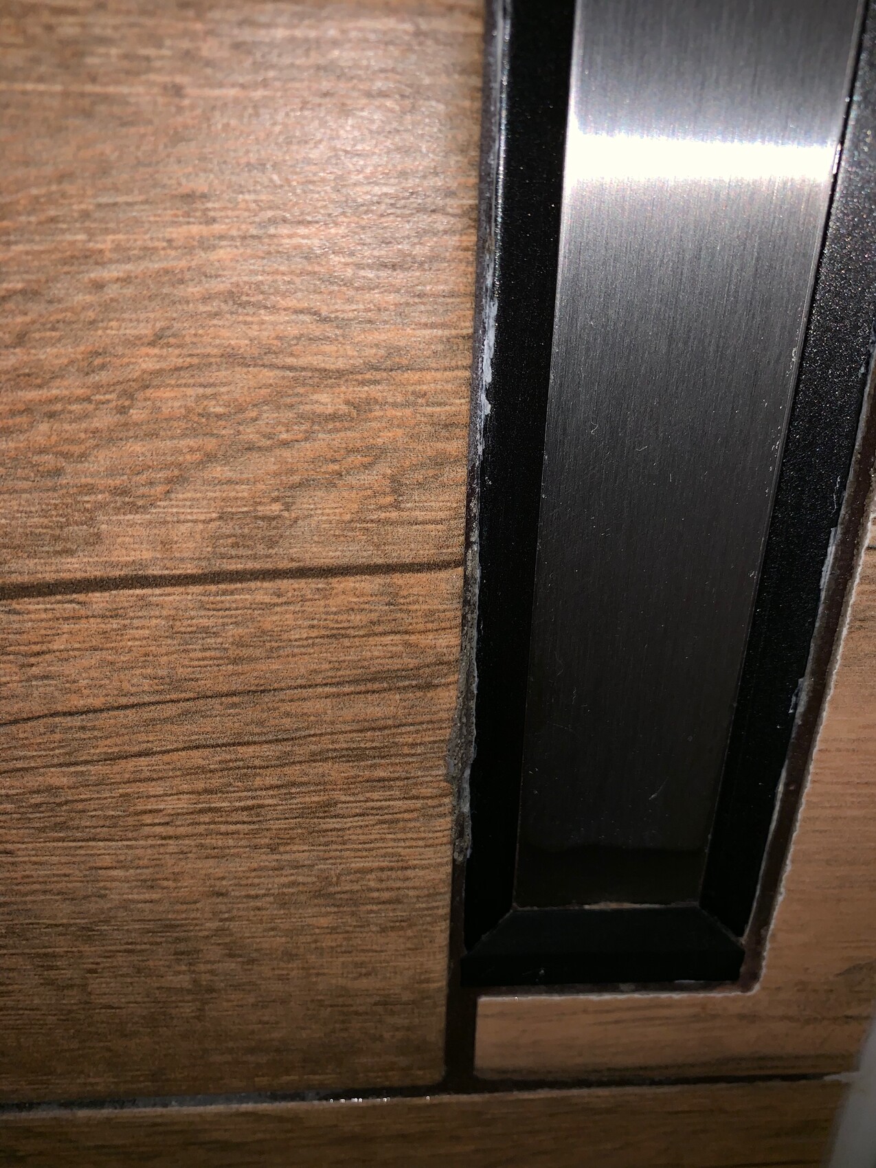Nahaufnahme eines Metallrahmens an der Holztuerkante mit sichtbarer Holzmaserung