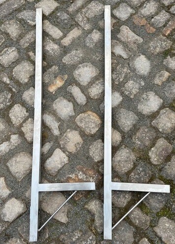 Zwei lange Metallrahmen liegen flach auf Kopfsteinpflaster.