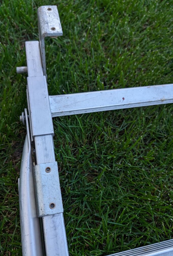 Nahaufnahme eines zusammenklappbaren Aluminiumrahmens mit Schraubenlöchern auf Gras.