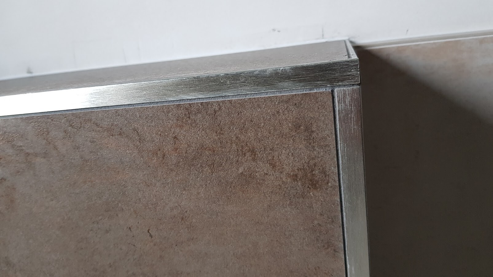 Nahaufnahme eines Metallrahmens mit braunem Paneel an einer Möbelkante.
