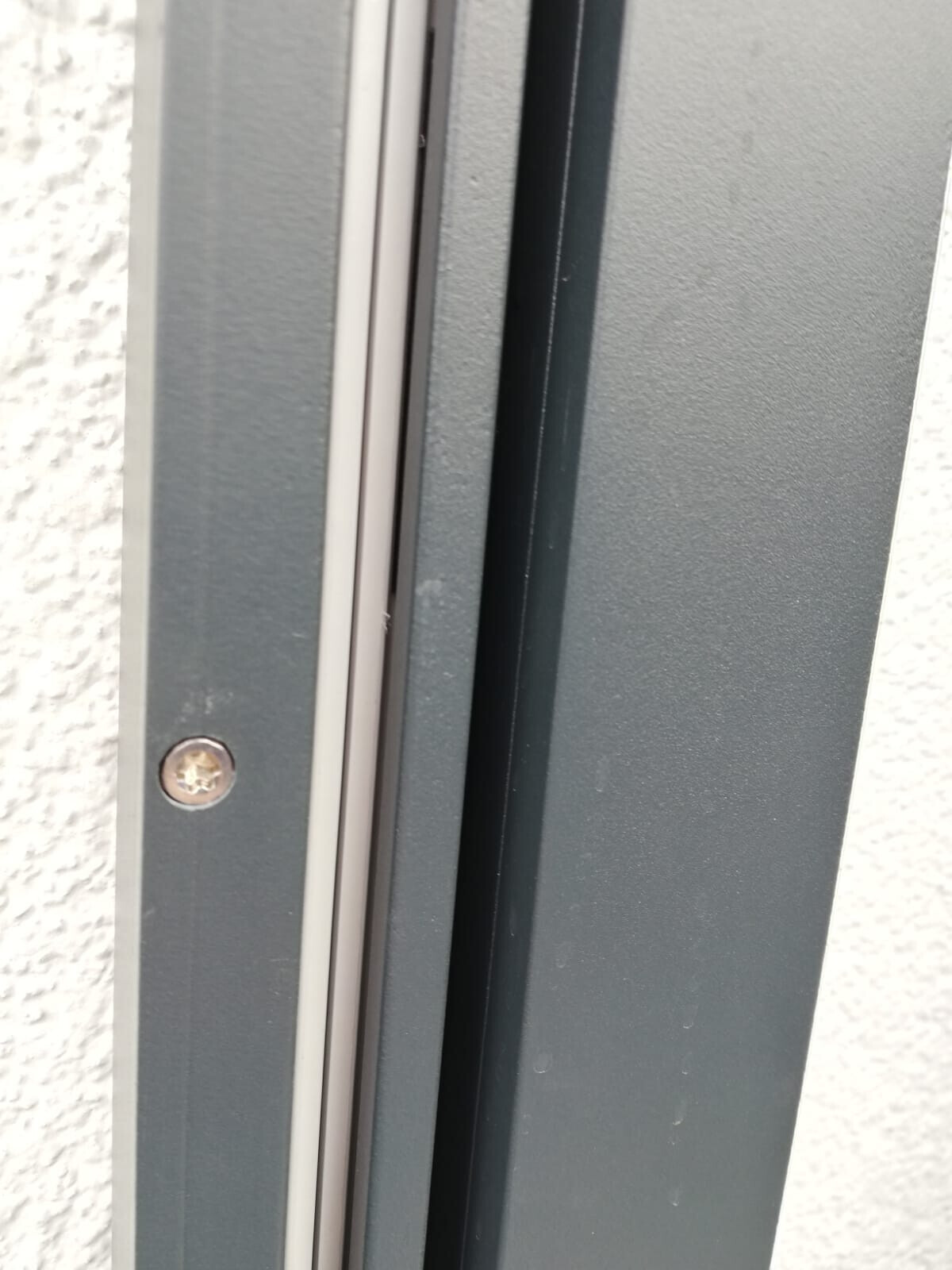 Nahaufnahme eines grauen Metallrahmens eines Fensters oder einer Tür, mit Dichtung und Schraube.