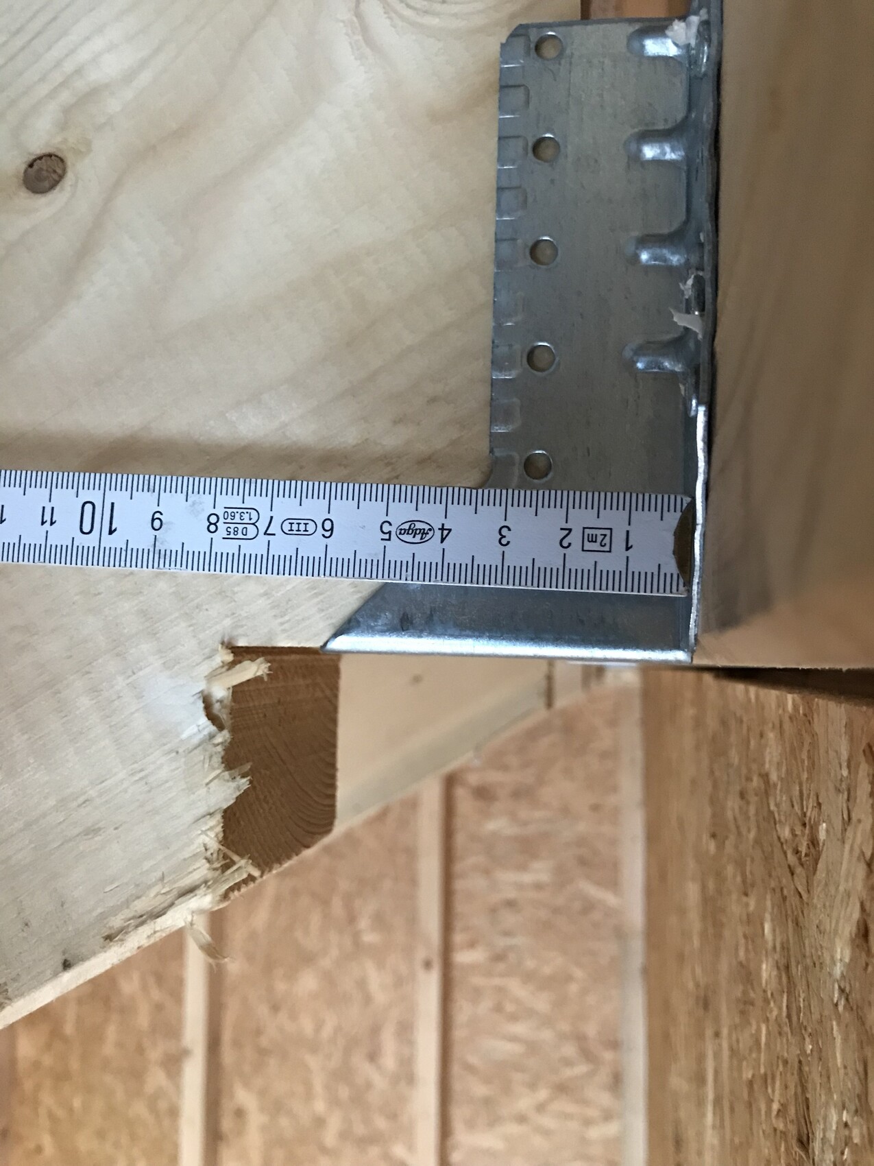Metallwinkel an Holzbalken, Maßband zeigt Abstand von ca. 9 cm zur Kante.