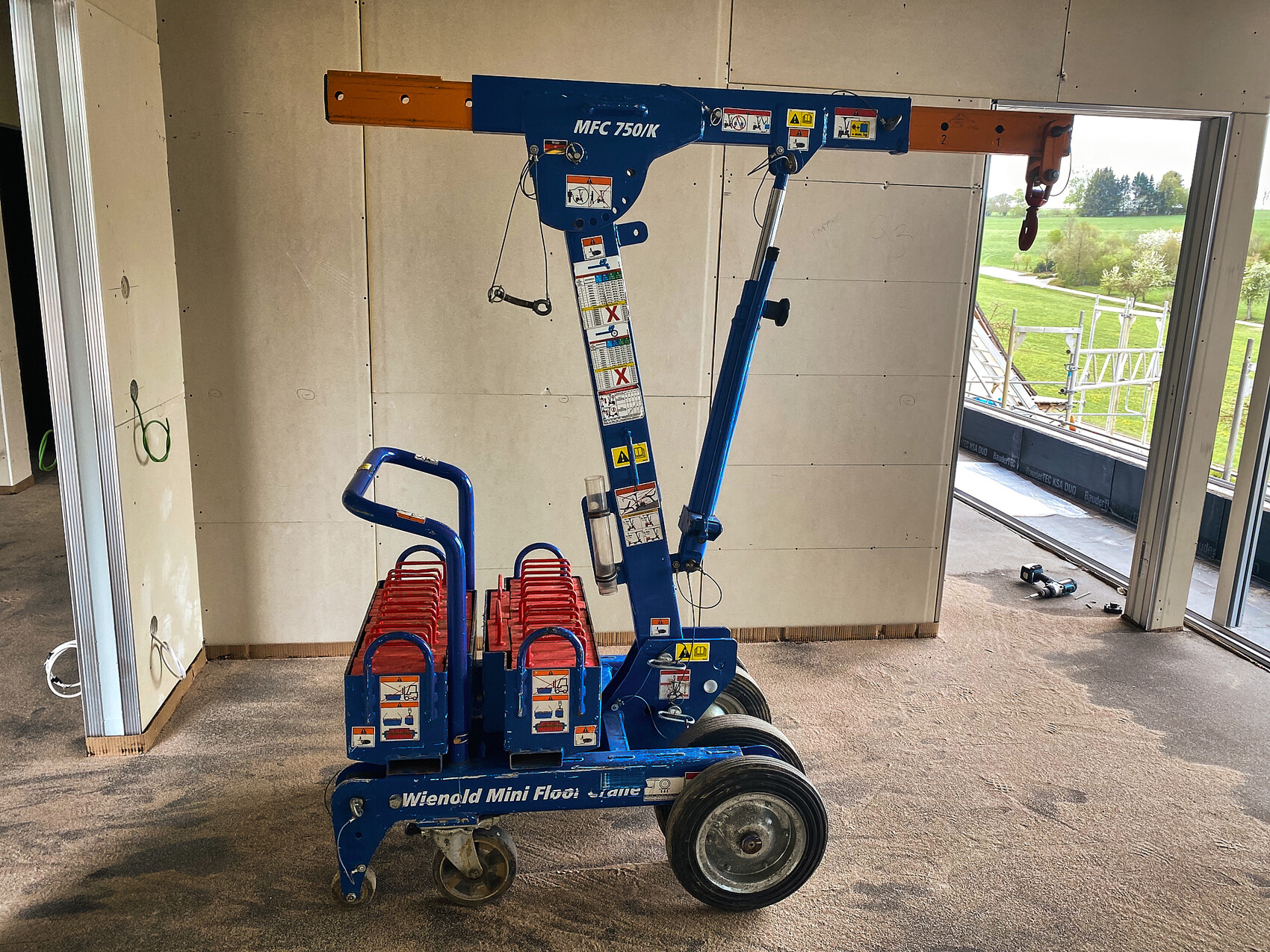 Kleiner mobiler Baukran auf einer Innenausbau-Baustelle mit Wandplatten und offener Fensteröffnung