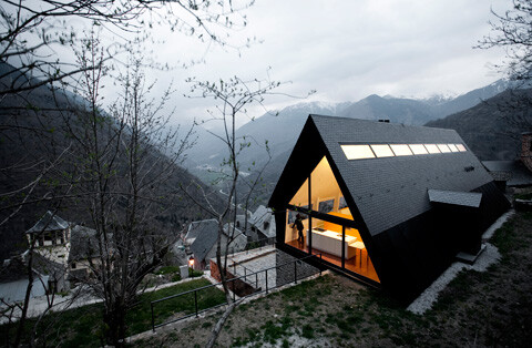 Modernes A-frame Haus mit großen Glasfronten auf Berghang und Berglandschaft