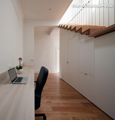 Moderner Arbeitsbereich mit Schreibtisch, Laptop, weißen Einbauschränken und Treppe aus Holz.