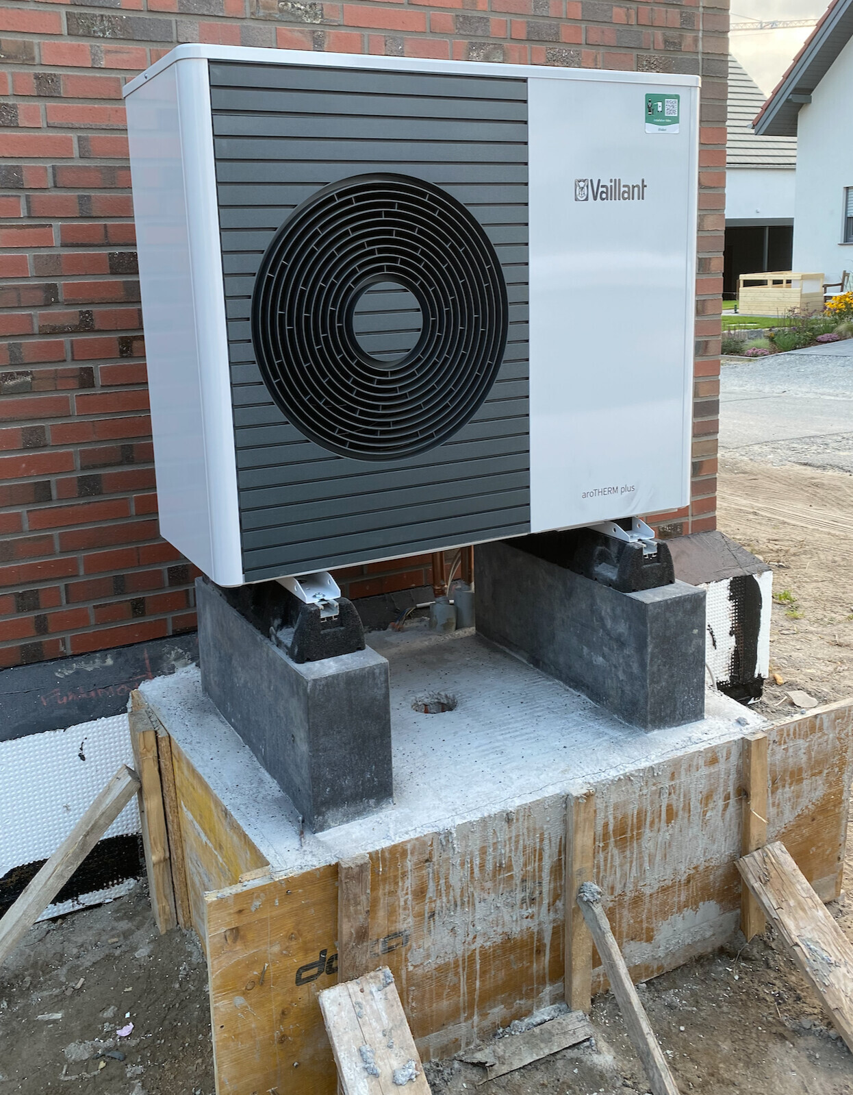 Vaillant aroTHERM Plus Außengerät mit großem Lüfter auf Betonfundament vor Ziegelhaus
