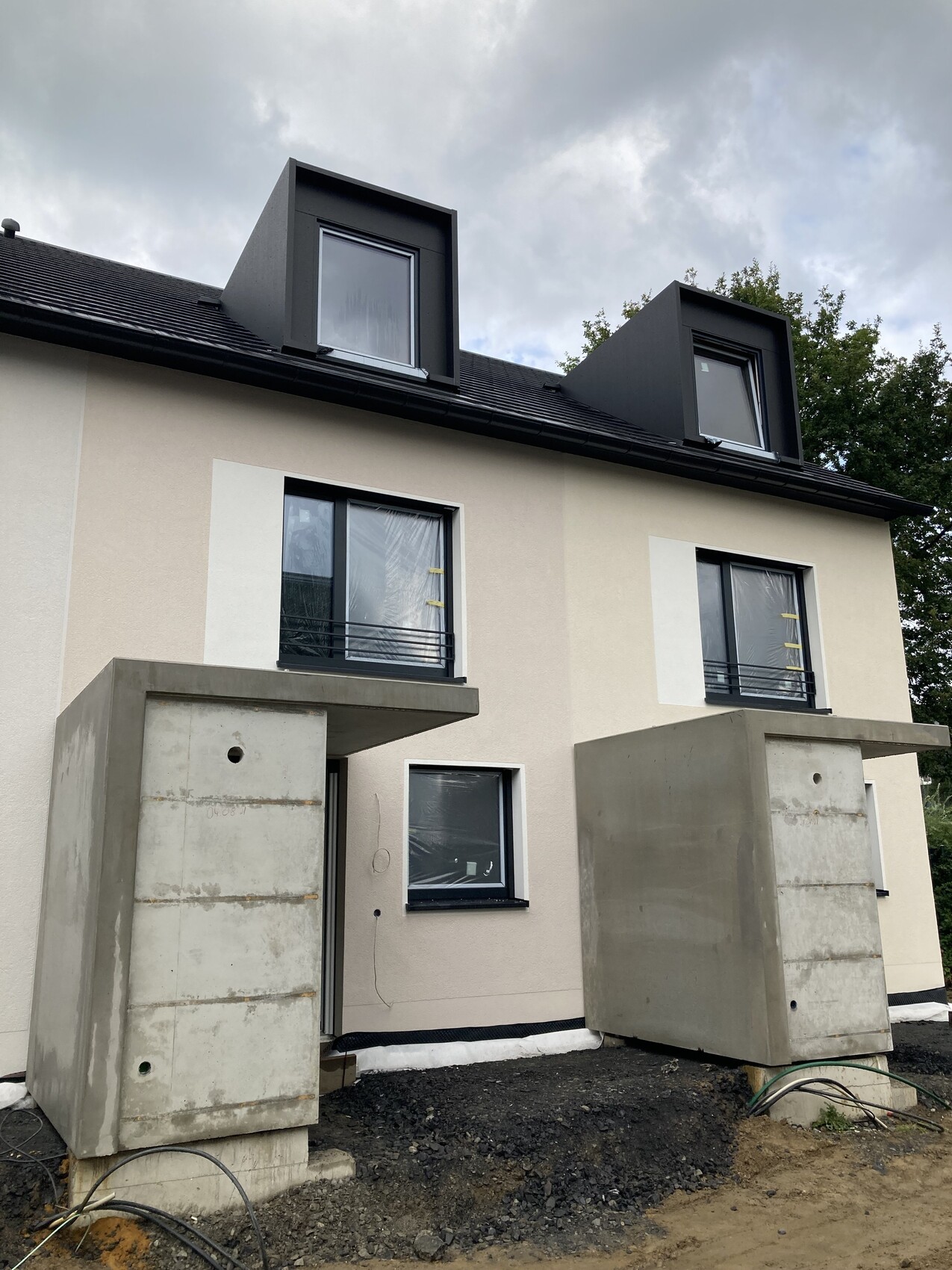 Neues Zweifamilienhaus im Bau mit Dachgauben und Betonfundamenten.