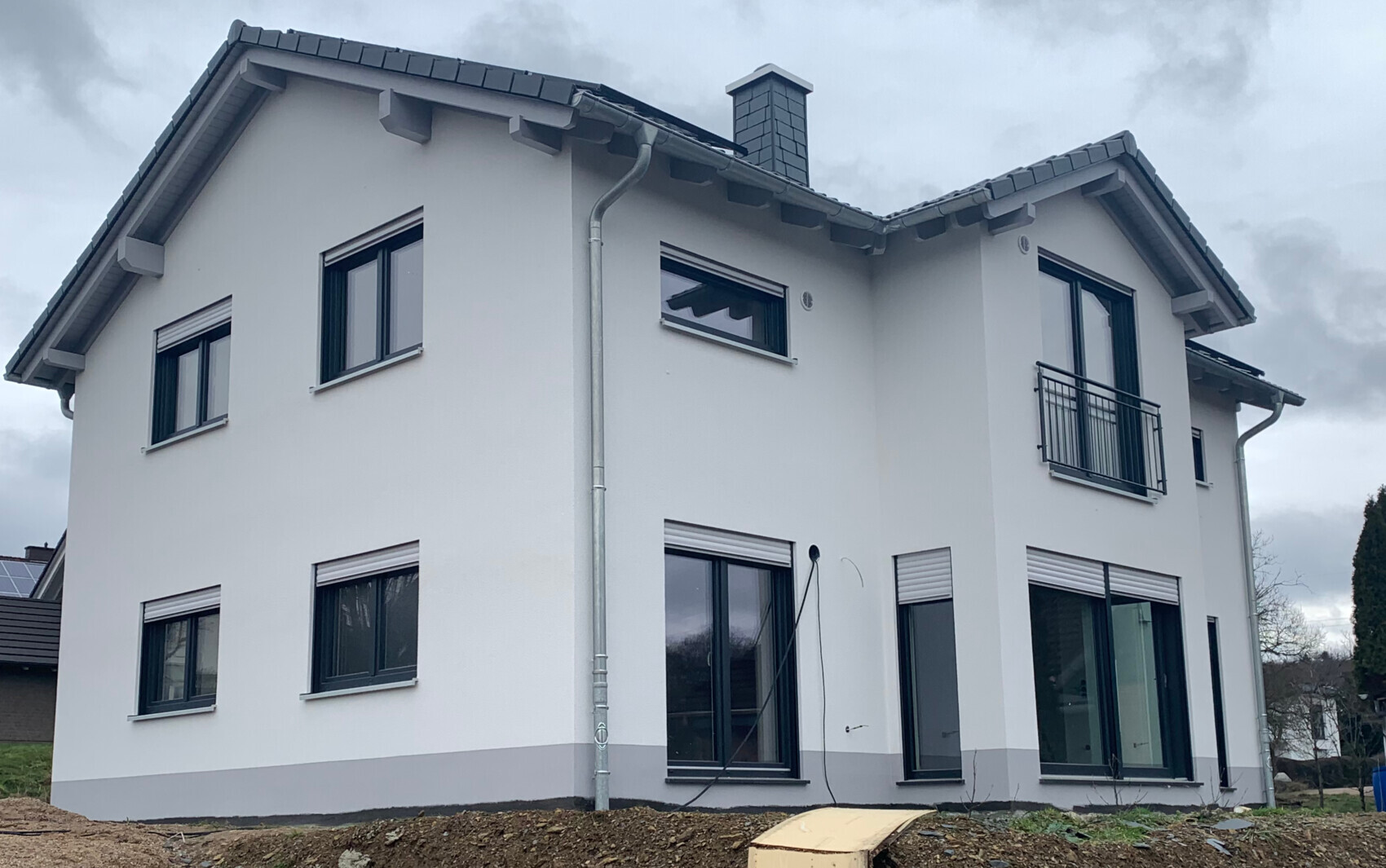 Modernes, weißes Einfamilienhaus mit großen Fensterfronten und Balkon rechts.