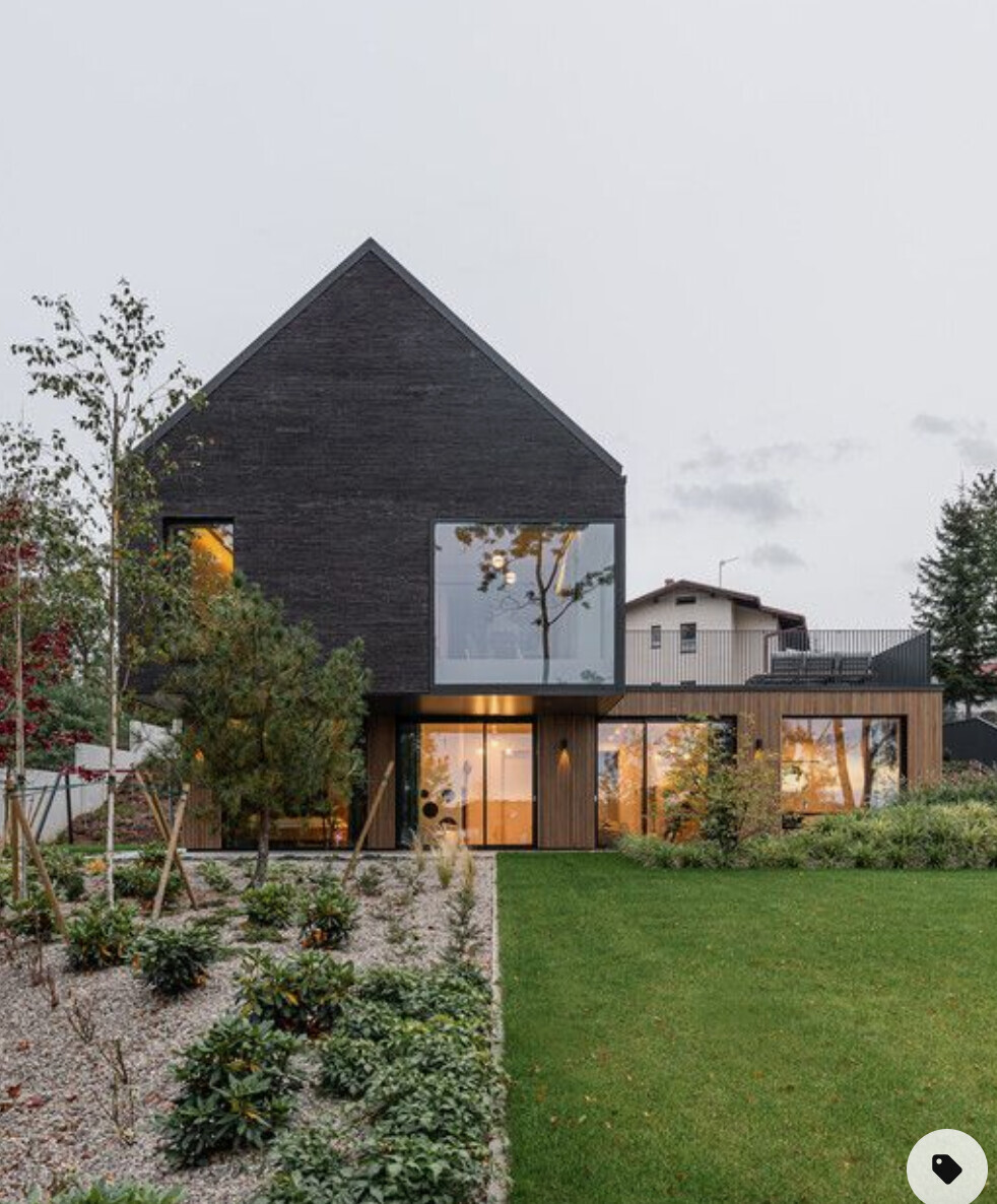 Modernes, zweigeschossiges Haus mit schwarzer Ziegel-Fassade und großen Fenstern im Garten.