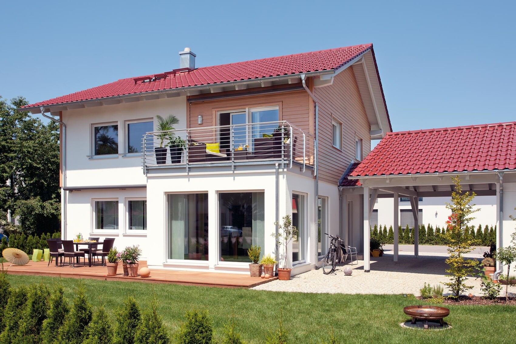 Modernes zweistöckiges Haus mit rotem Ziegeldach, Balkon, Terrasse, Garten und Carport.