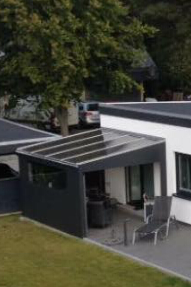 Moderne Hausfront mit überdachter Terrasse, Outdoor-Möbeln und Gartenbereich.