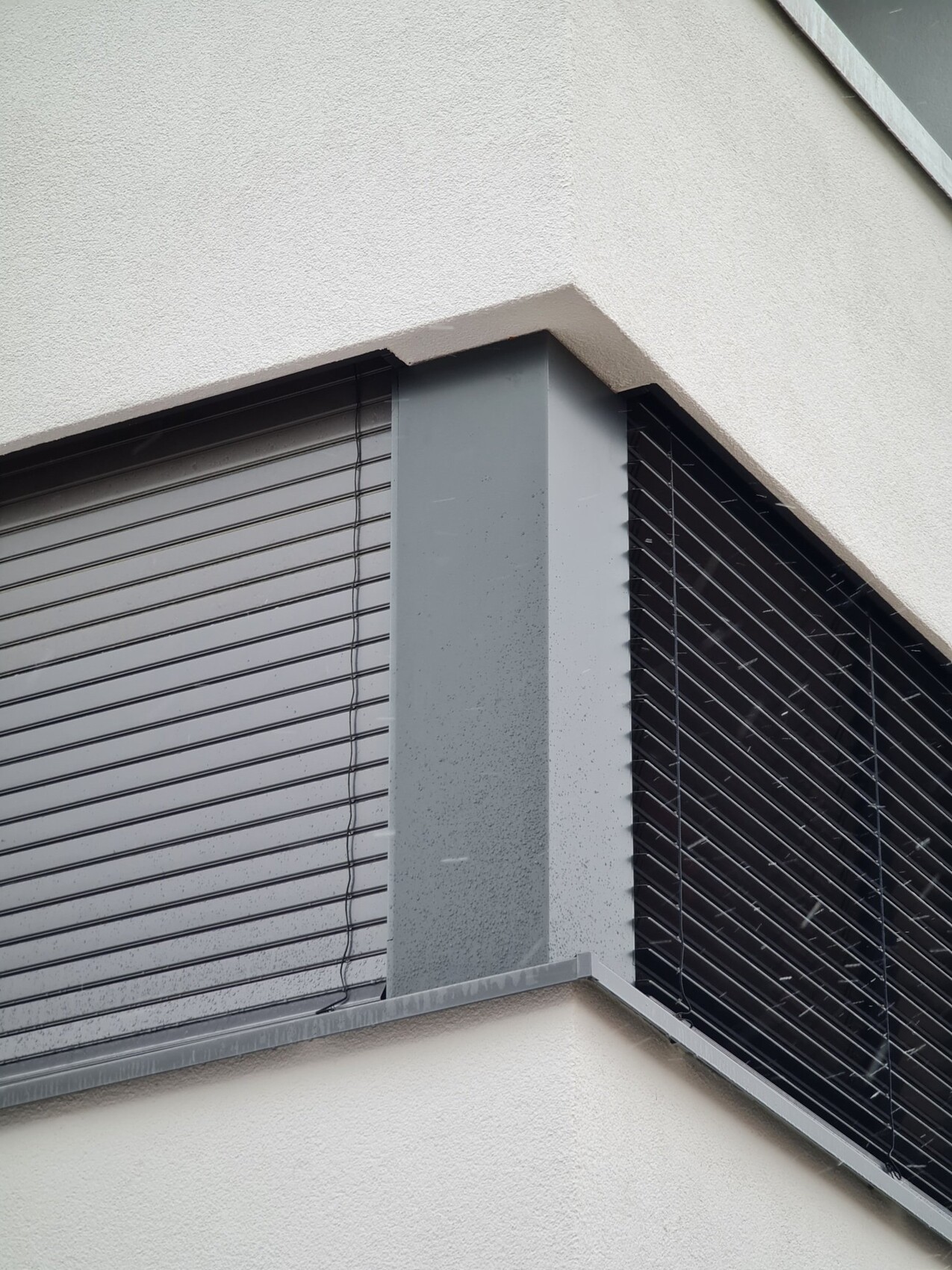 Außenfassade mit Fensterecke, geschlossenen Jalousien und grauem Metallrahmen