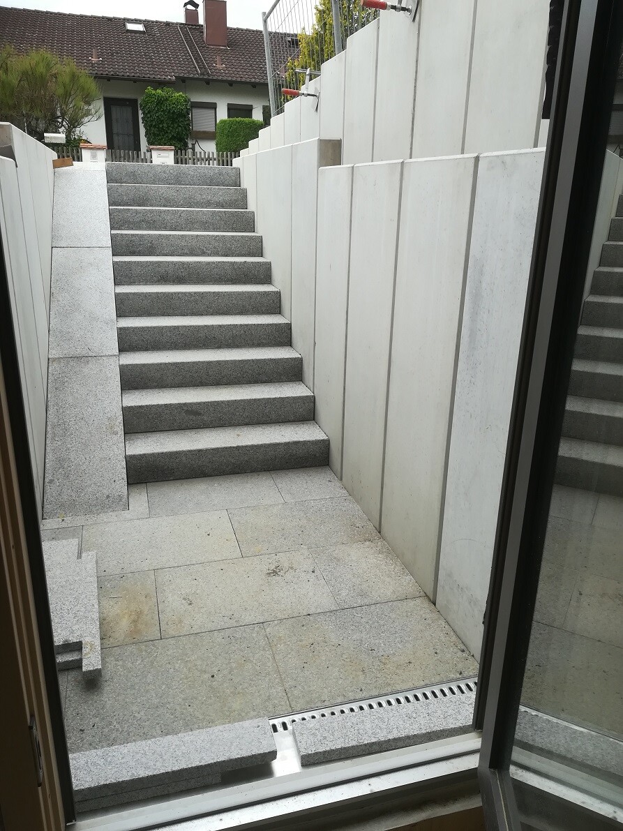 Außenstufen aus grauem Stein führen zwischen hohen Betonwänden zu einer Treppe zum Haus.