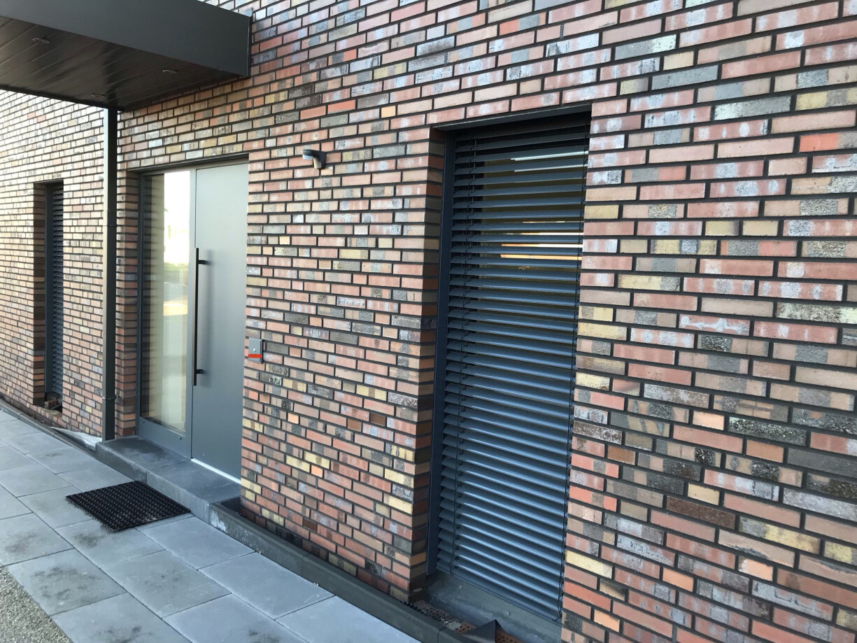 Außenansicht eines modernen Backsteingebäudes mit Glastür und Rollladenfenster.