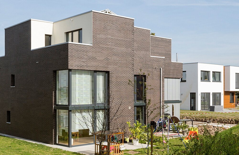 Moderne Wohnhäuser aus braunem Backstein mit großen Glasfronten; Spielplatz im Garten.