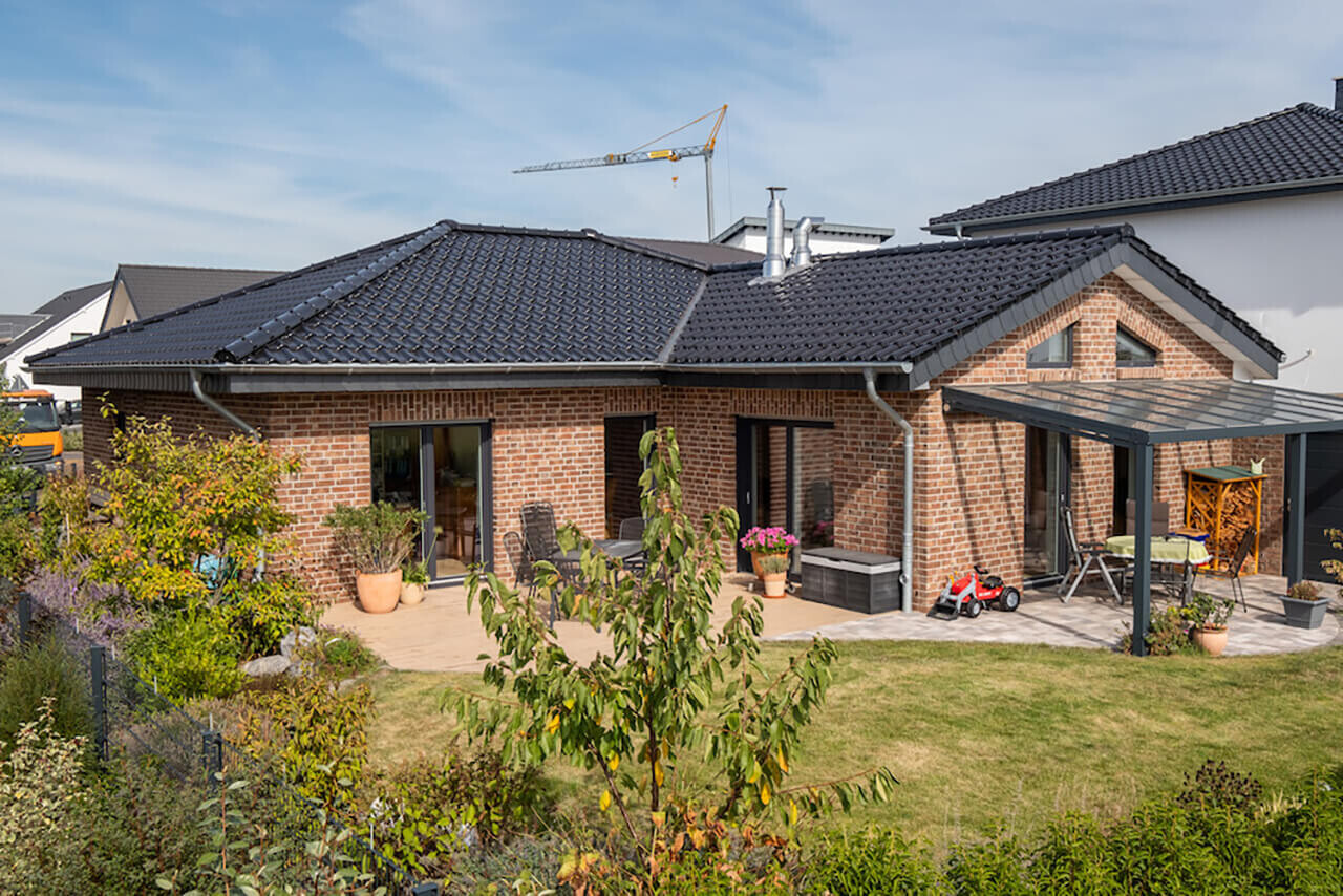 Ziegelhaus mit dunklem Dach, Terrasse und Garten; Kran im Hintergrund