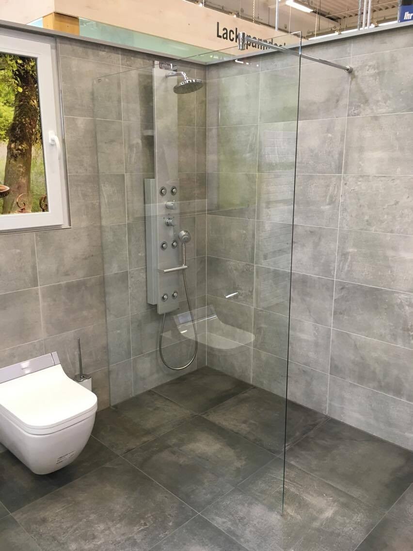 Moderne Dusche mit Glasabtrennung, Wandduschpaneel und Toilette in grauem Bad.