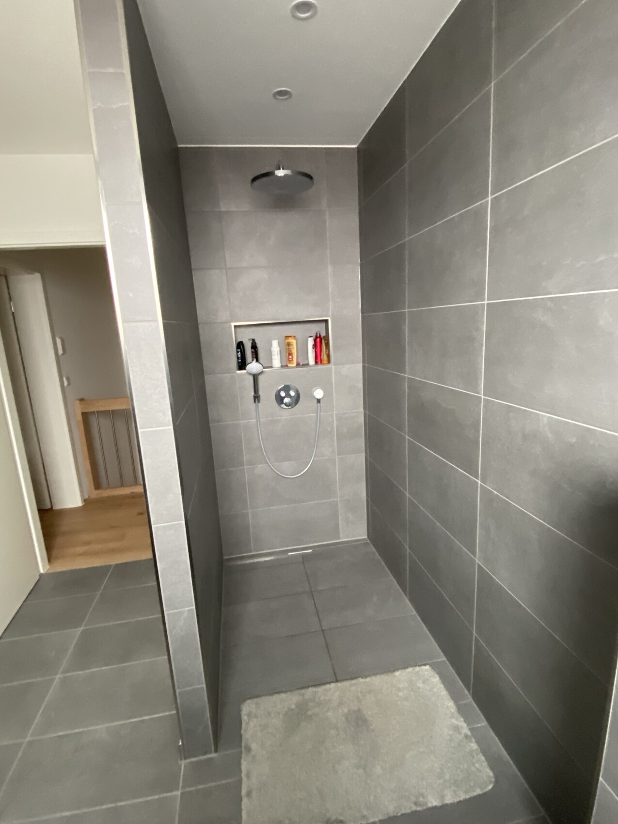 Moderne graue Dusche mit Deckenregenduschkopf, Handbrause und Nische mit Pflegeprodukten.