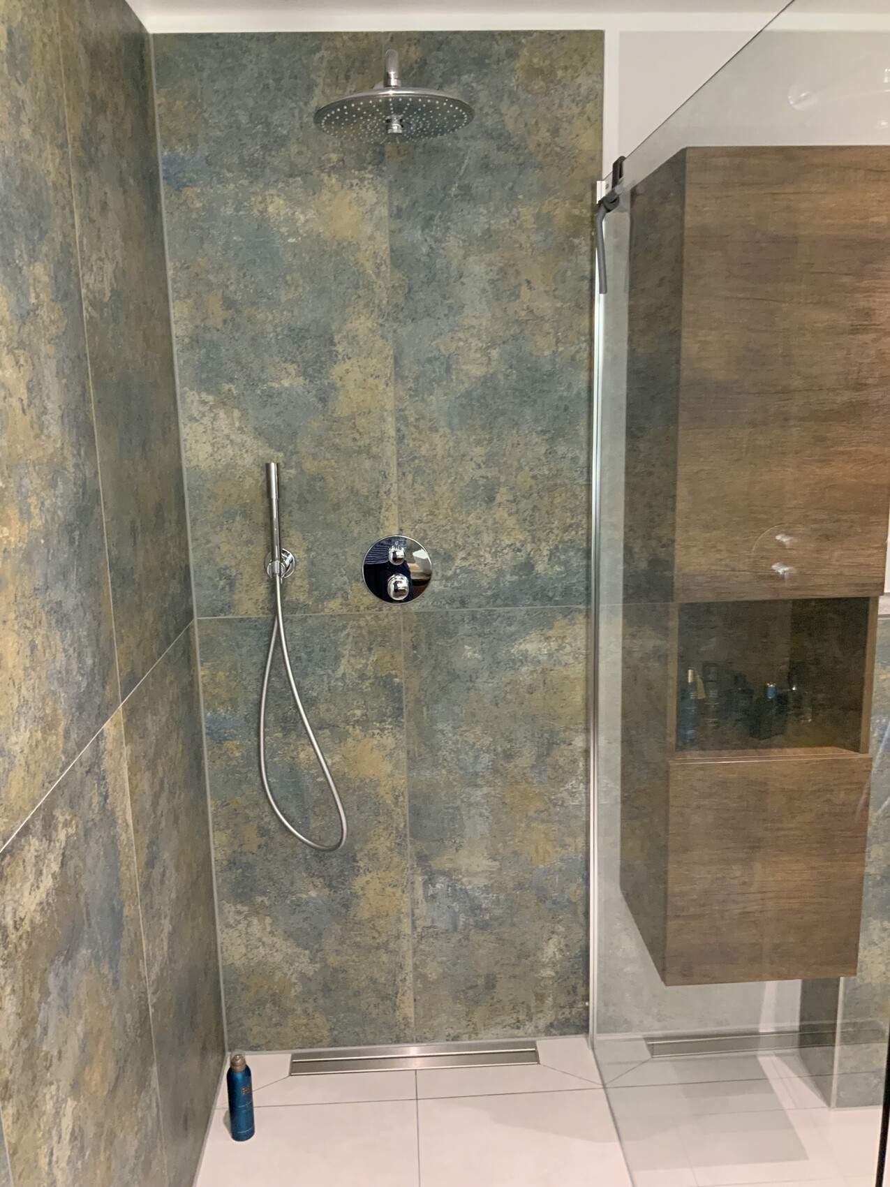 Moderner Duschbereich mit Regenkopf, Handbrause, Glasabtrennung und Holzschrank an der Seite.