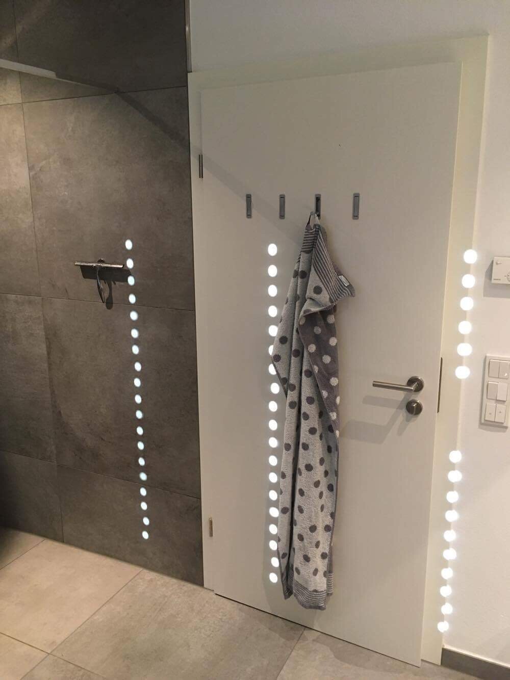 Weiße Tür im Badezimmer mit Haken, graues gepunktetes Handtuch hängt daran.