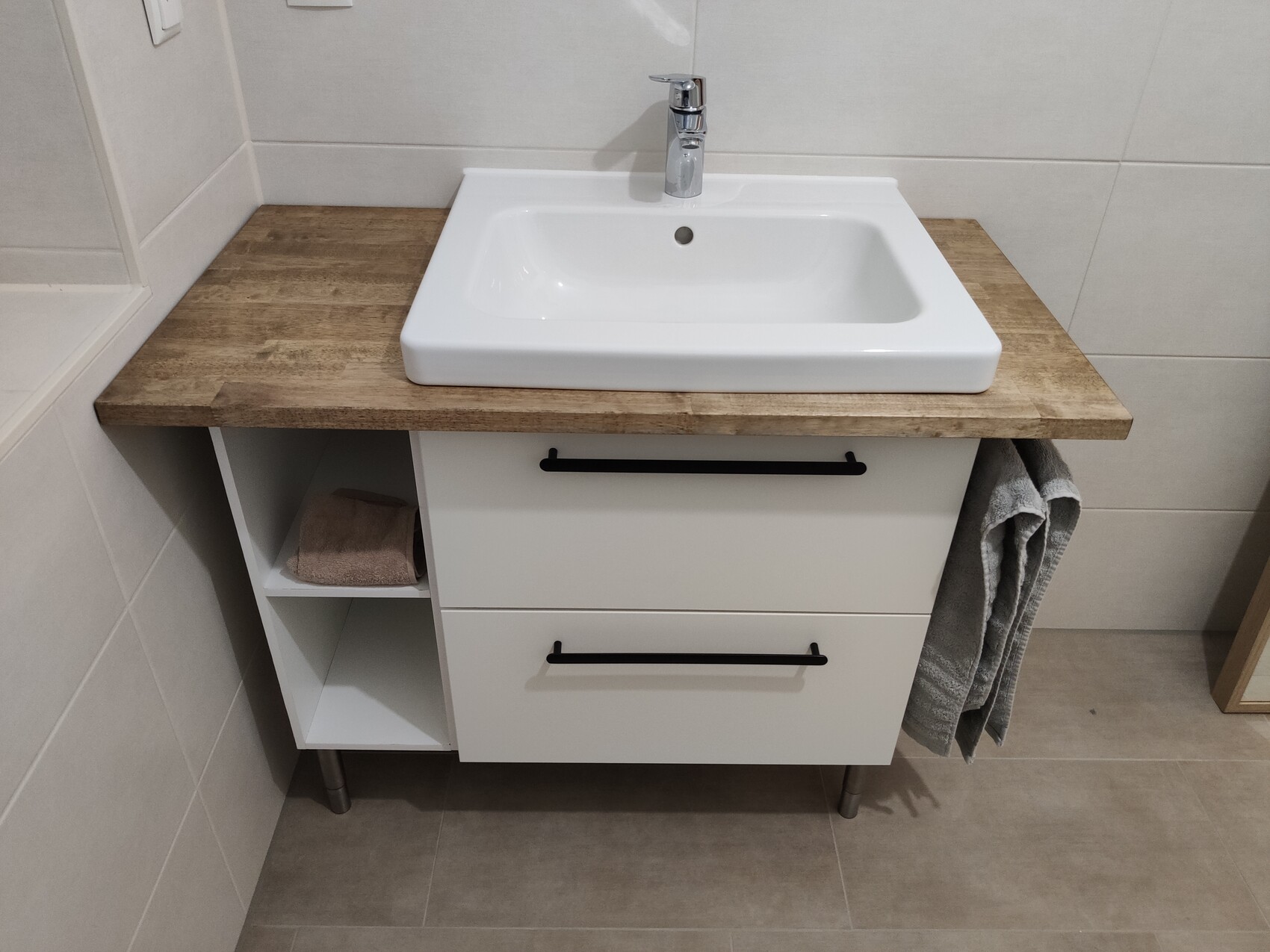 Waschbecken auf Holztisch, weiße Schubladen mit schwarzen Griffen, Handtuch rechts.