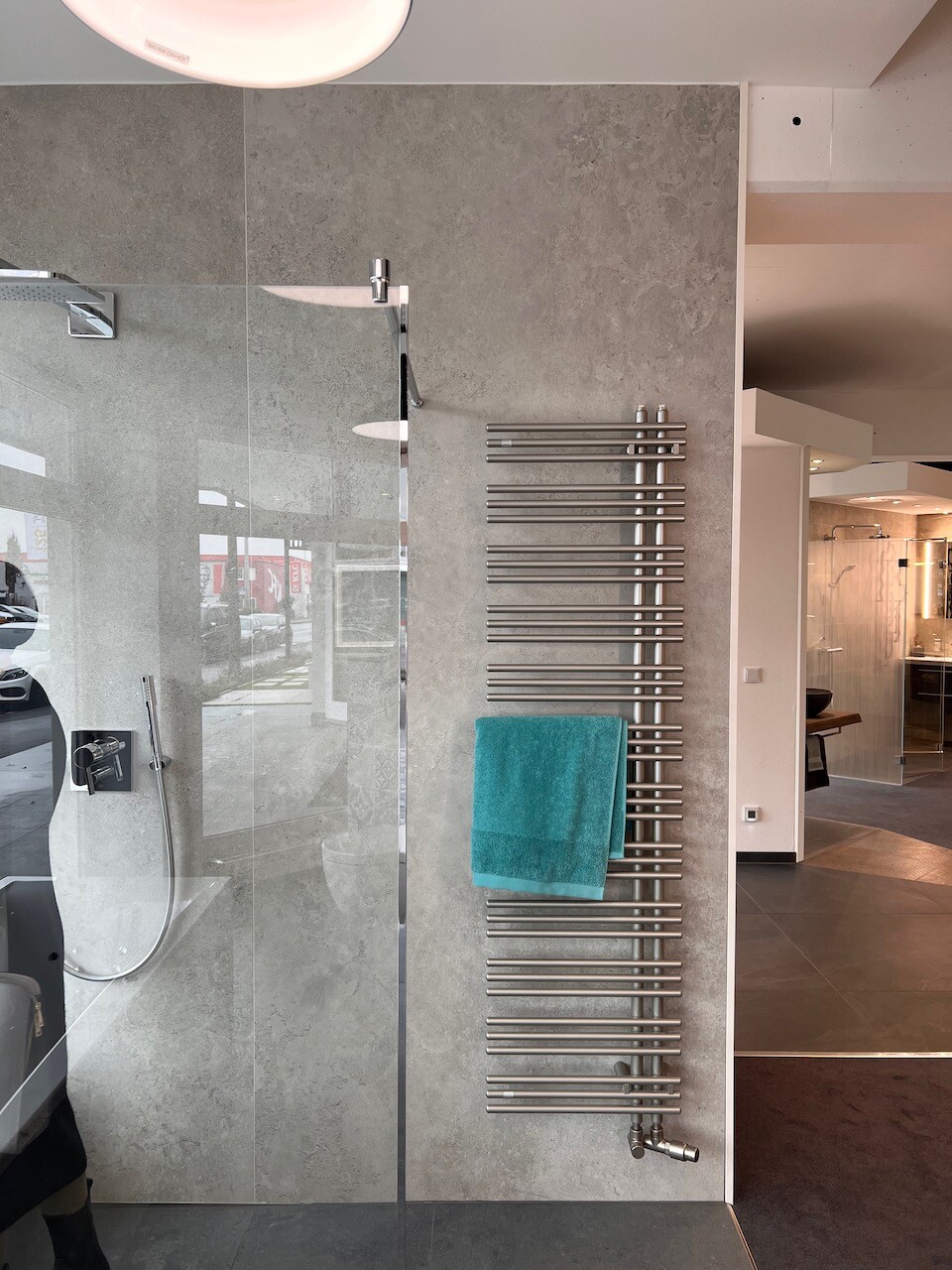 Moderne Dusche mit Glaswand links, neben Heizkörper mit türkisfarbenem Handtuch.