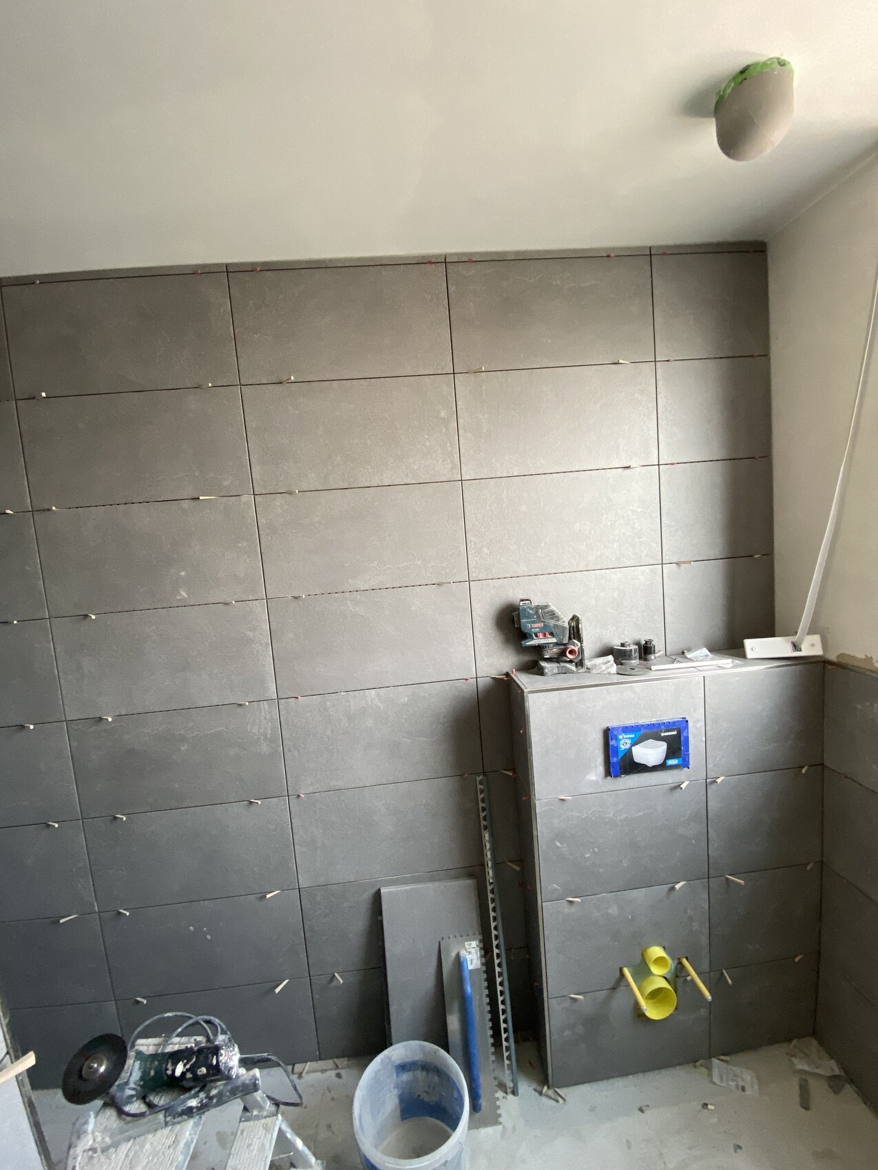 Bauzimmer mit grau gefliester Wand, Werkzeugen und Fliesenarbeiten.