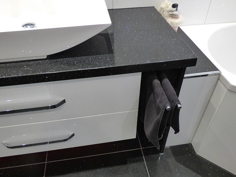 Badezimmer: schwarze Glitzer-Graniteplatte, Waschbecken links, graue Handtücher am Schrank, Plüschbär.