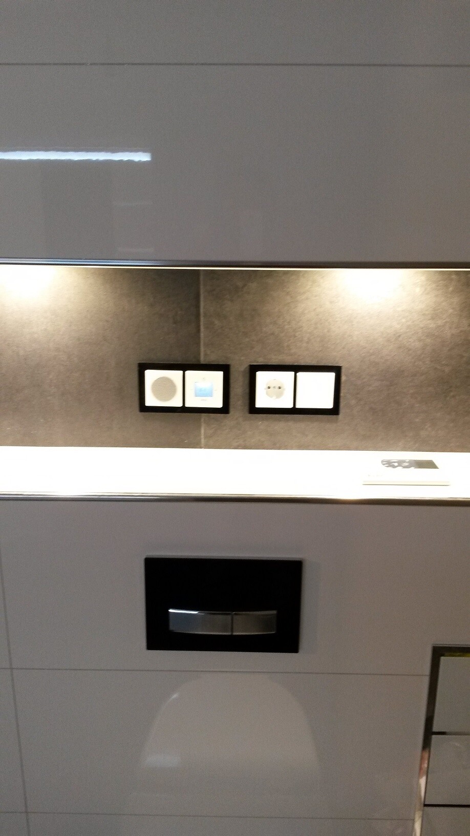 Moderne Badezimmerwand mit grauer Glasoberfläche, verstecktem Spülkasten und Steckdosen