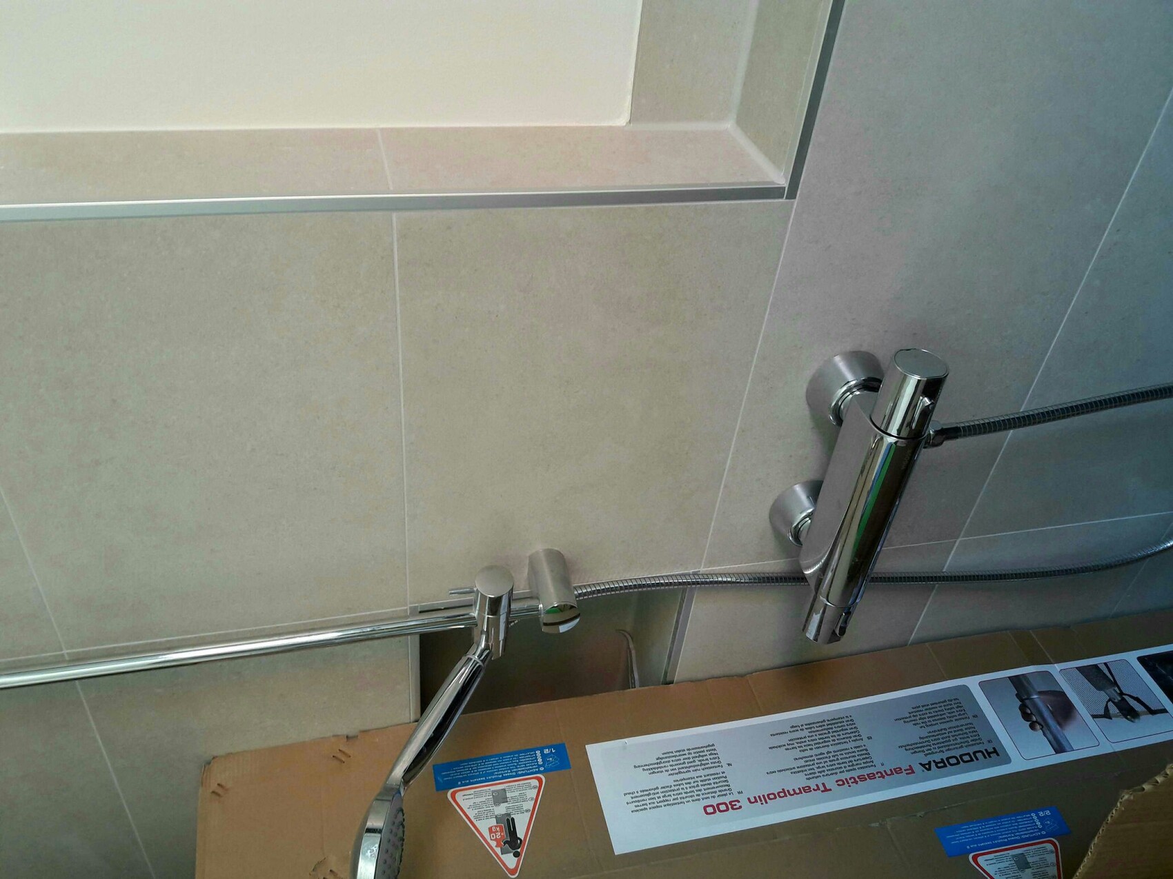 Chrom-Duschearmatur mit Handbrause an beigefarbenen Fliesen im Bad.