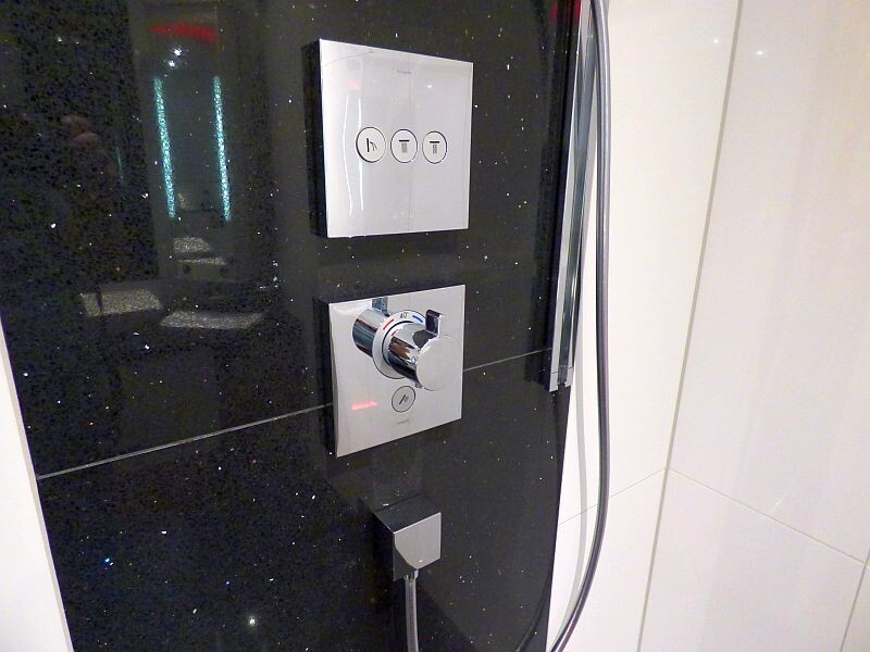 Moderne Badarmatur mit Duschknopf an schwarzem Wandpaneel im Badezimmer.