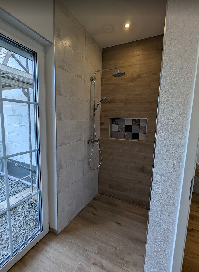 Walk-in-Dusche mit Regendusche und Handbrause, Holzoptik-Wand und integrierter Mosaik-Nische.