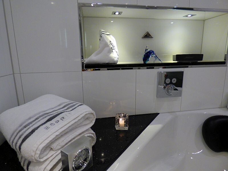 Badezimmer mit weißen Handtüchern, Kerze und Spiegel über schwarzer Ablage an der Badewanne.