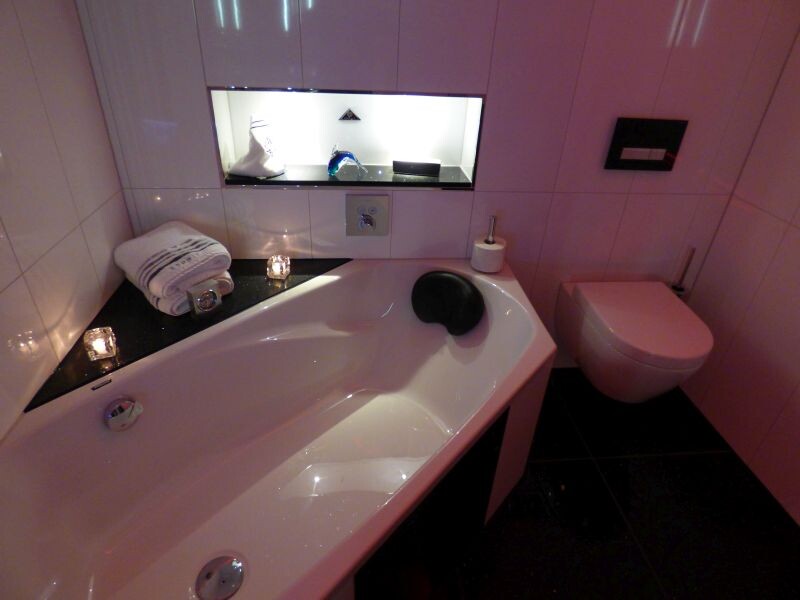 Modernes Badezimmer mit Eckbadewanne, Kerzen, Handtuchstapel und Wandtoilette.