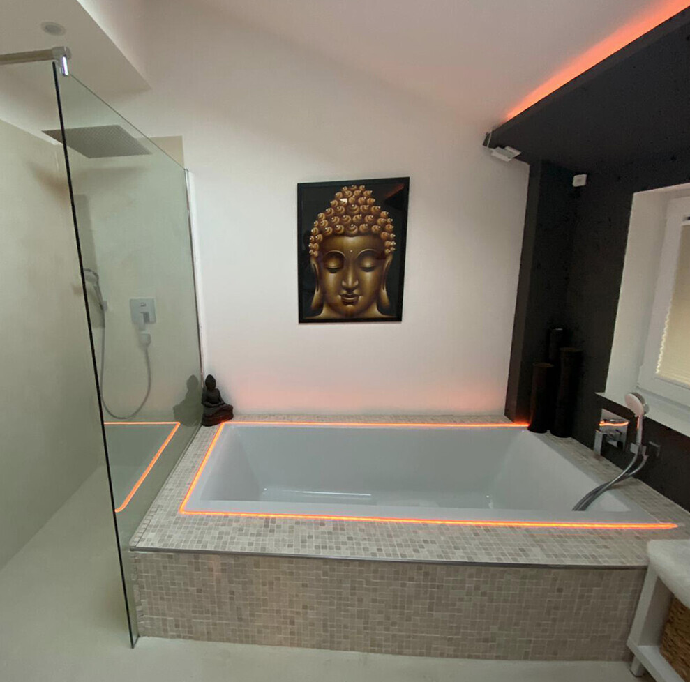 Moderne Badewanne mit orange LED-Beleuchtung, Glasdusche links, Buddha-Gemälde an der Wand.