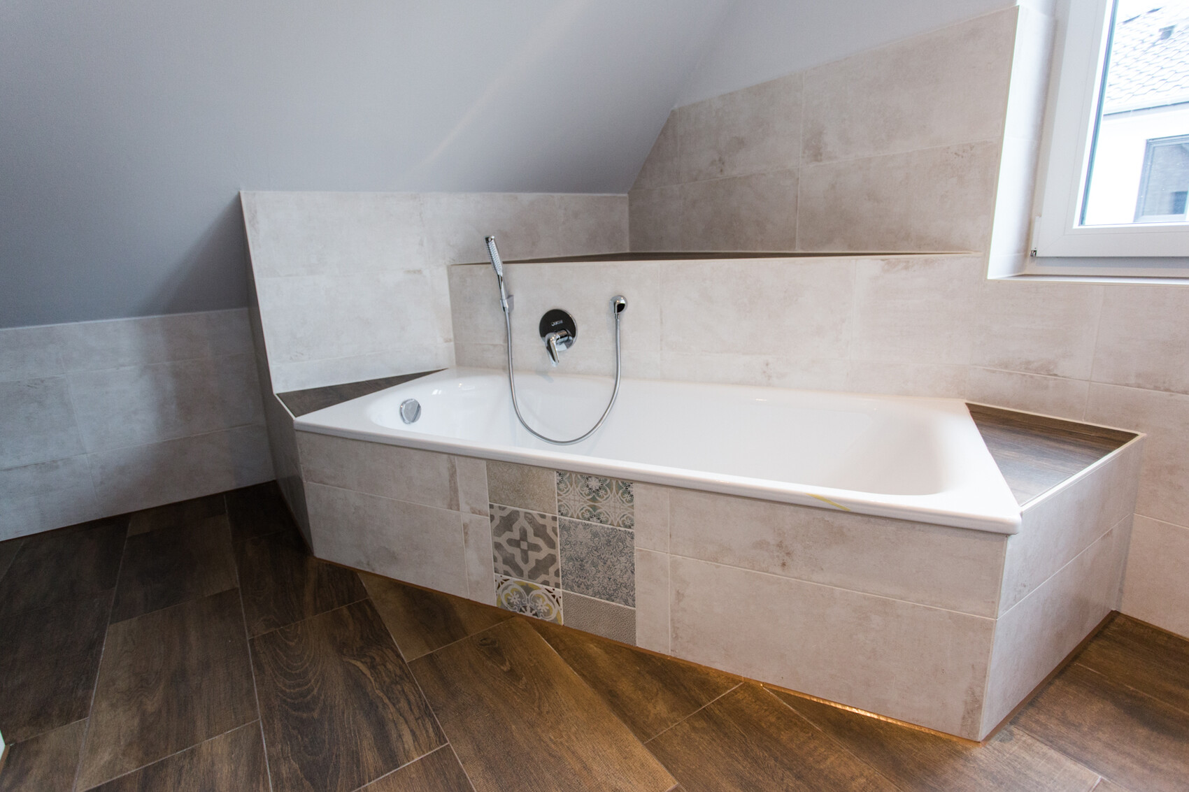 Moderne Badewanne in beigen Fliesen, Handbrause, am Fenster, Holzboden.
