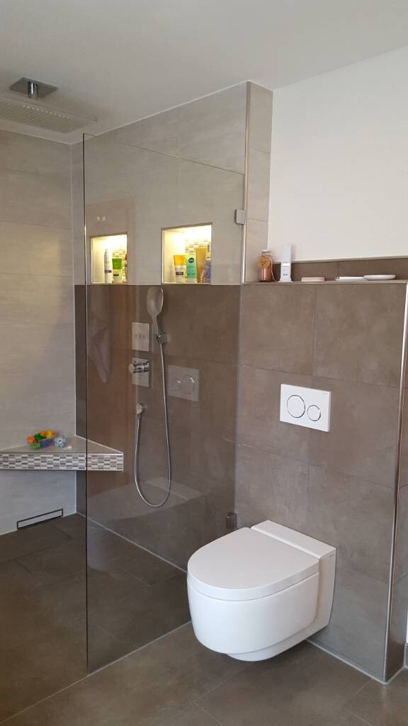 Modernes Badezimmer mit Glasdusche, Wand-WC, Nischenbeleuchtung und grauen Fliesen.