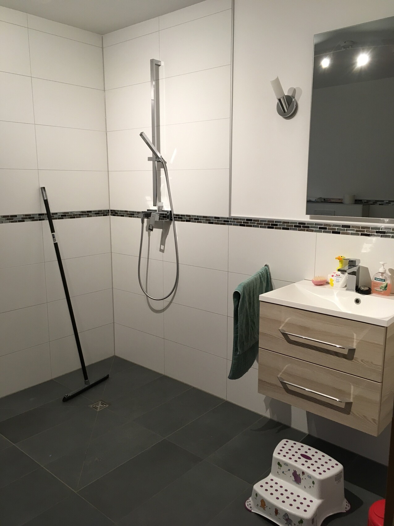 Modernes Badezimmer mit Dusche, Waschtisch, Spiegel, Handtuch und kleinem Trittleiter.