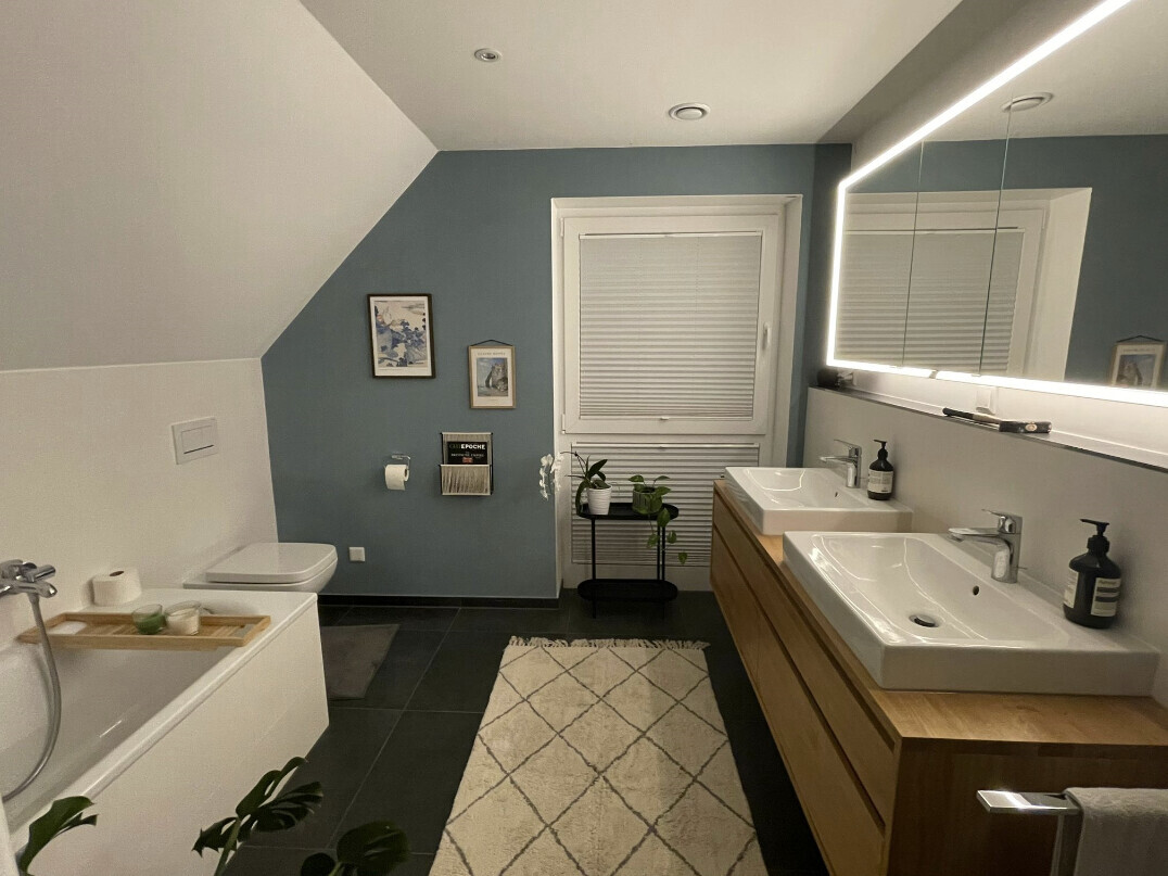 Badezimmer mit blauer Akzentwand, Doppelwaschbecken, Badewanne, Toilette und LED-Spiegel