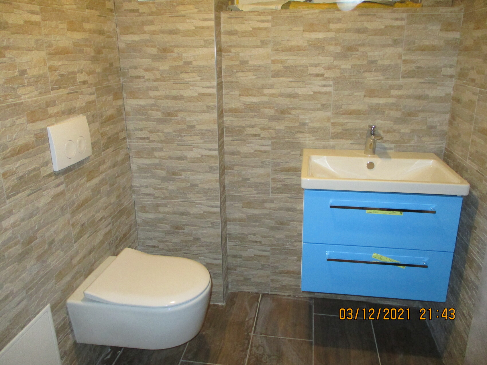 Badezimmer mit wandhängendem WC, blauem Waschtischunterschrank und Waschbecken.