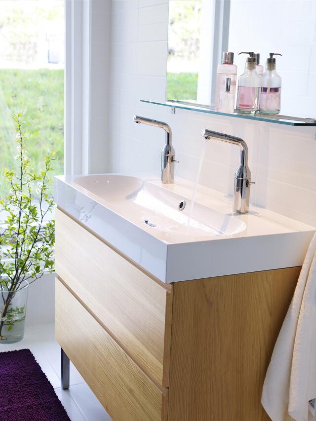 Moderner Waschtisch mit zwei Armaturen, Glasablage, Seifenspendern und Holzunterschrank