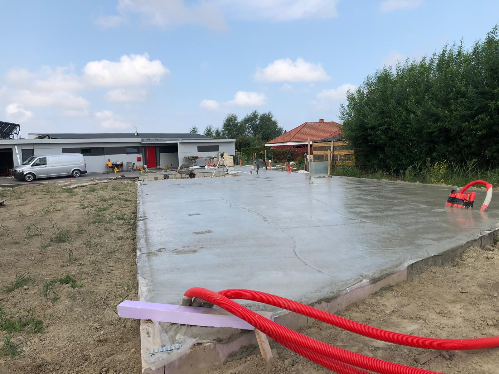Frisch gegossene Betonplatte auf einer Baustelle, Van, Arbeiter und Gebäude im Hintergrund.