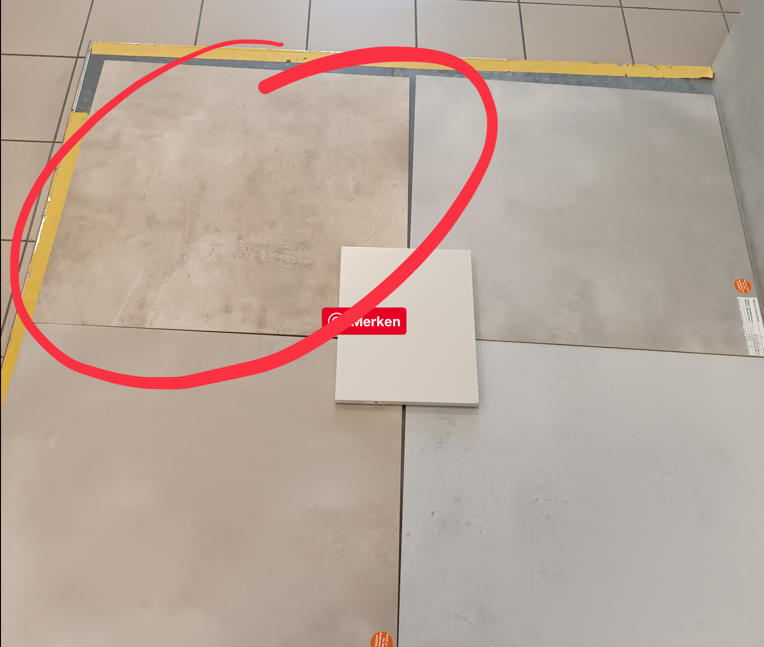 Ausstellungsboden mit beige- und grauen Fliesen; in der Mitte weiße Kachel mit rotem Aufkleber.