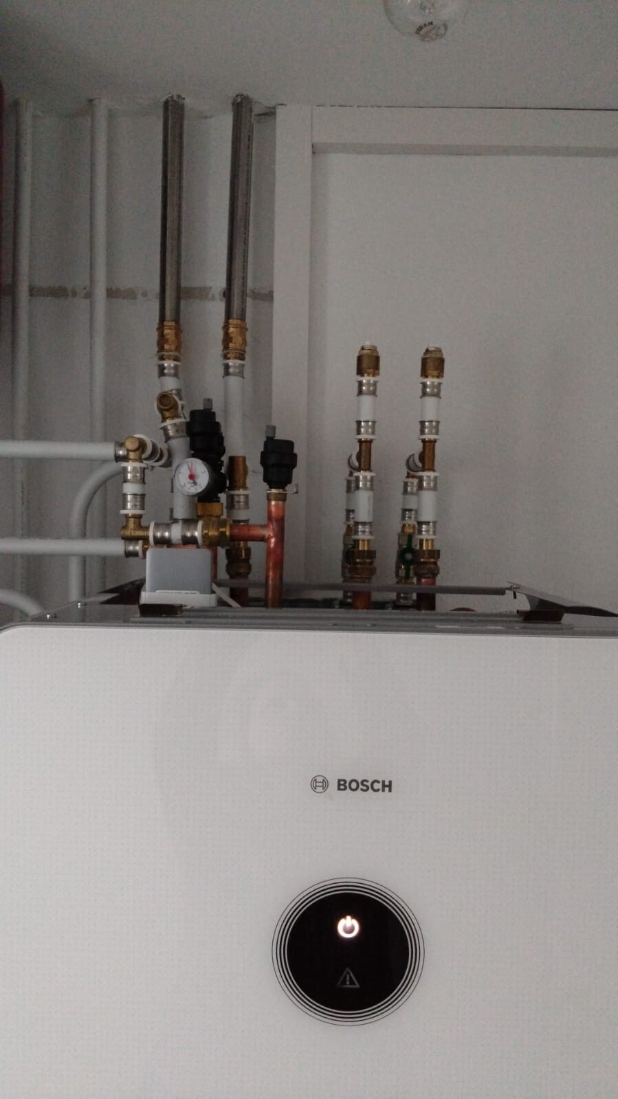 Bosch-Heizgerät mit sichtbaren Rohrleitungen, Manometer und rundem Bedienfeld.