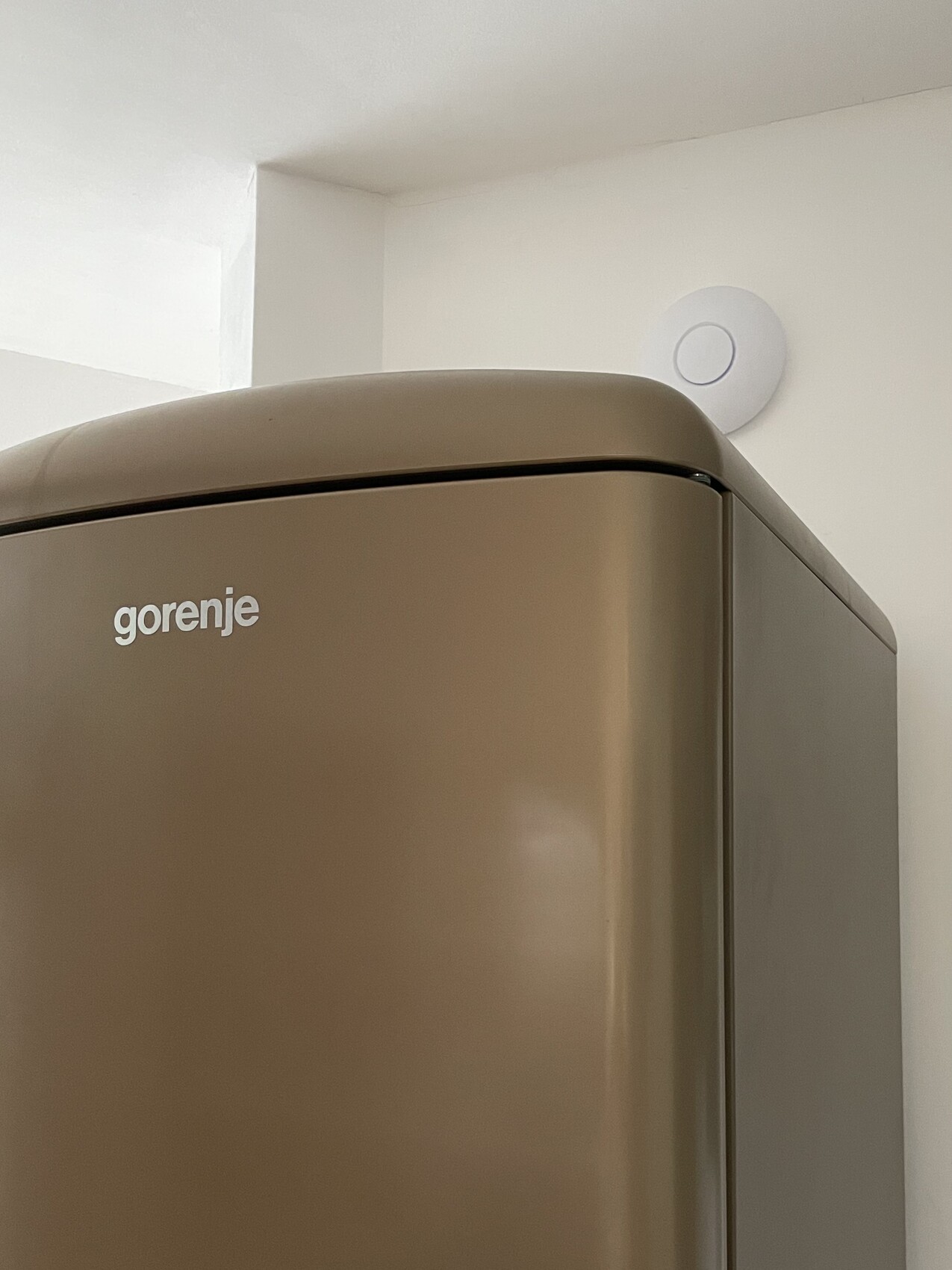 Gorenje Kühlschrank in Bronze-Ton neben einer weißen Wand mit rundem Rauchmelder.