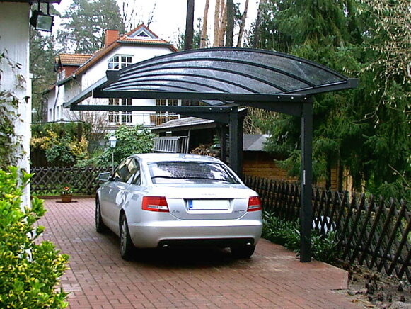 Silberner Wagen steht unter einer modernen Carport-Überdachung auf gepflasterter Einfahrt.