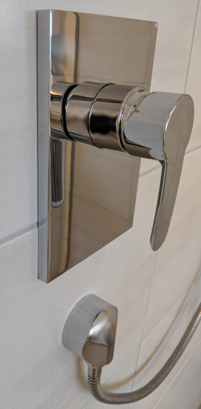 Moderne chromierte Duscharmatur mit Hebelgriff auf quadratischer Wandplatte und Brauseschlauch.