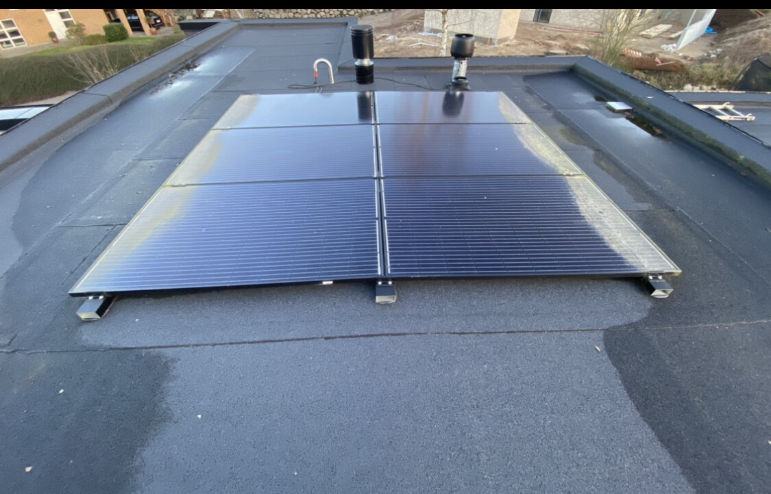Zwei Solarpaneele auf Flachdach, montiert auf Metallhaltern; Dachfläche im Fokus.