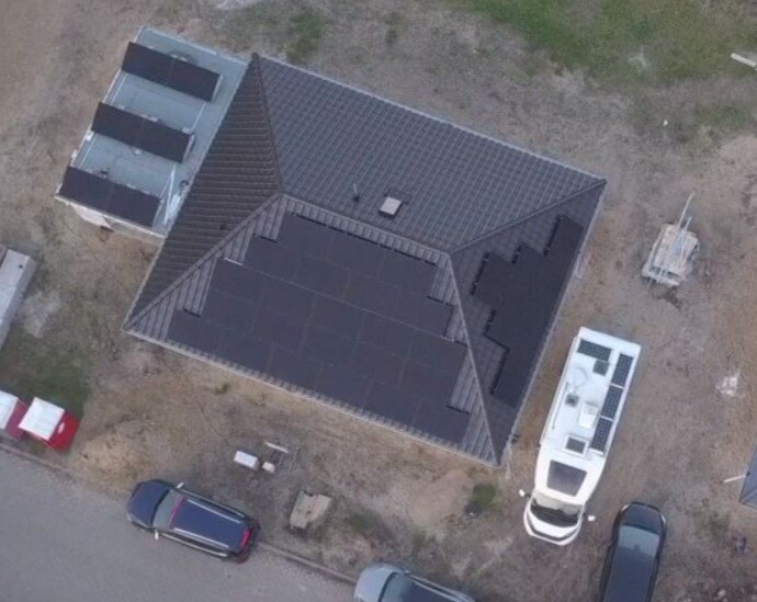 Drohnenaufnahme eines Hauses mit Solarmodulen auf dem Dach; davor stehen Autos und ein Wohnmobil.